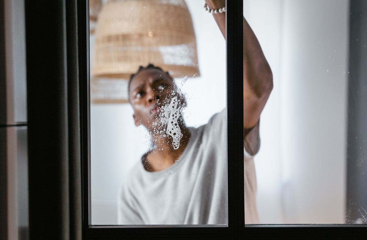 Un homme adulte nettoie une vitre à l’intérieur, en se concentrant sur les tâches ménagères et la propreté.