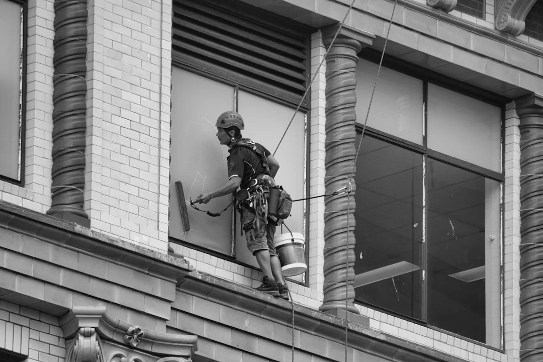 Deux techniciens nettoient les vitres d’un immeuble vitré depuis une plateforme élévatrice, afin d’améliorer l’esthétique du bâtiment.